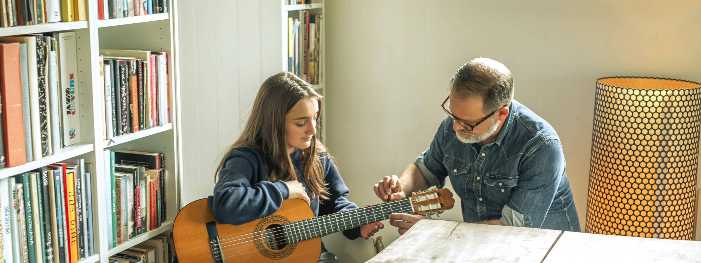 Ung pige sidder med en guitar, mens en lærer sidder ved siden af