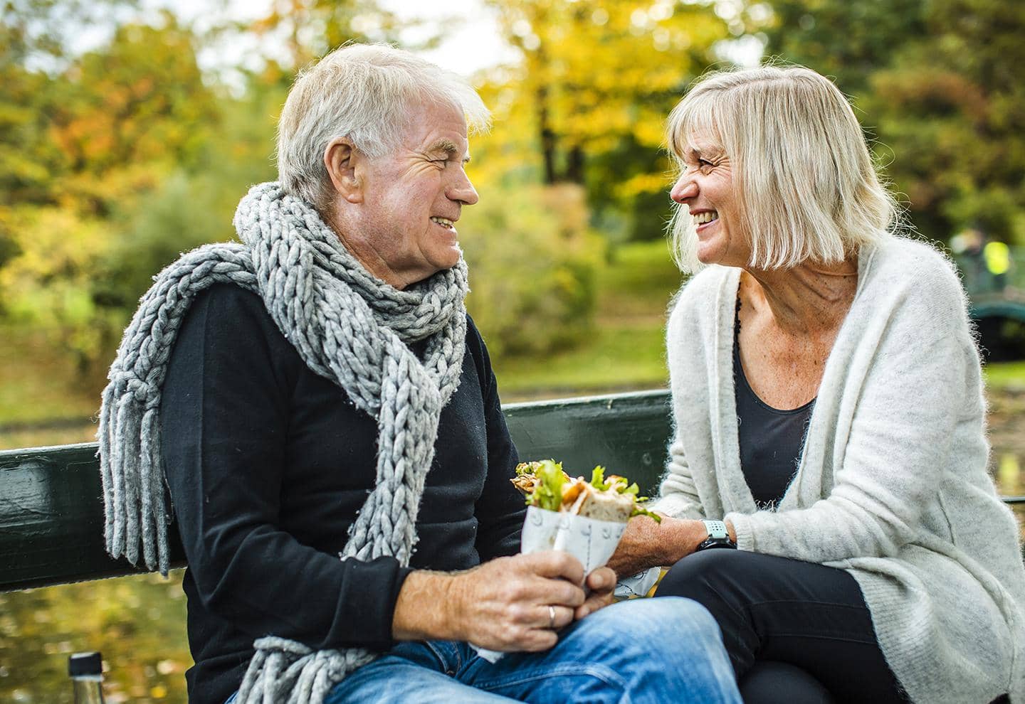 Ældre par sidder på bænk og smiler til hinanden, fotografi
