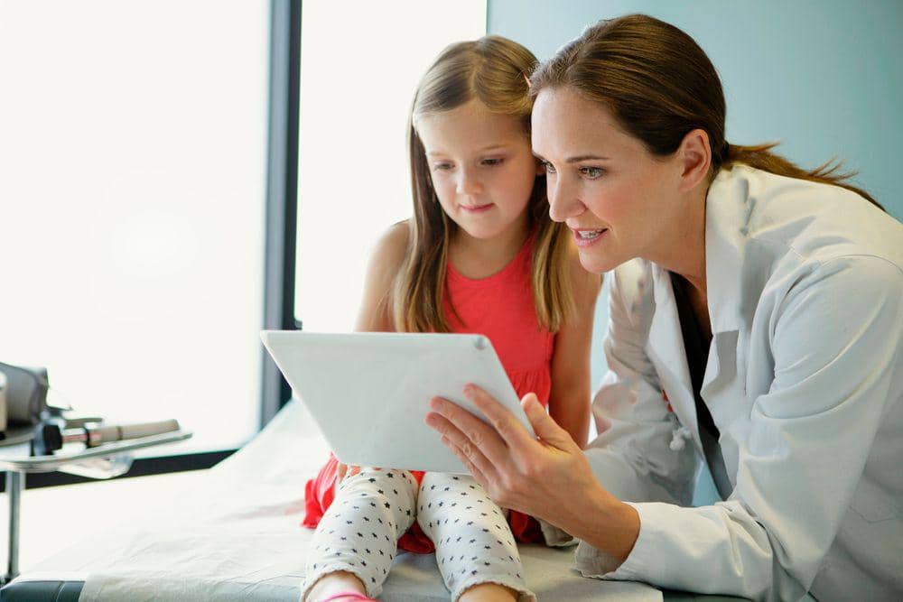 Læge viser en tablet til en lille pige på en klinik