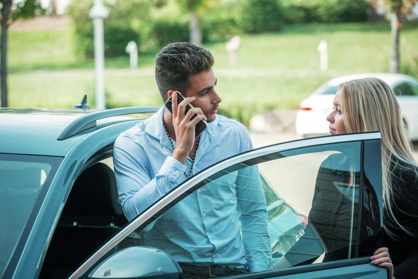Mand står og taler i telefon ved sin bil