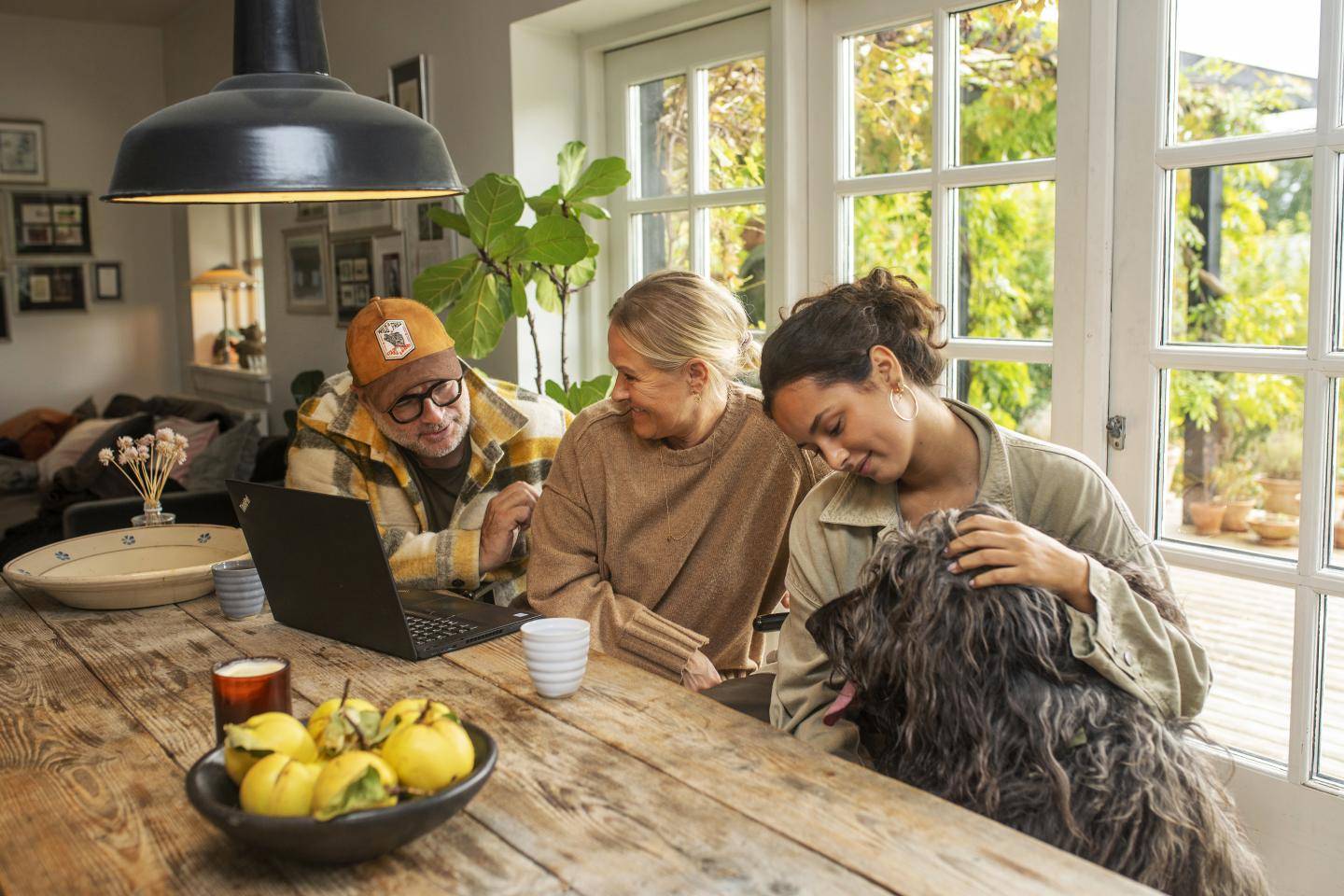 Familie sidder ved spisebord og smiler med hund, fotografi