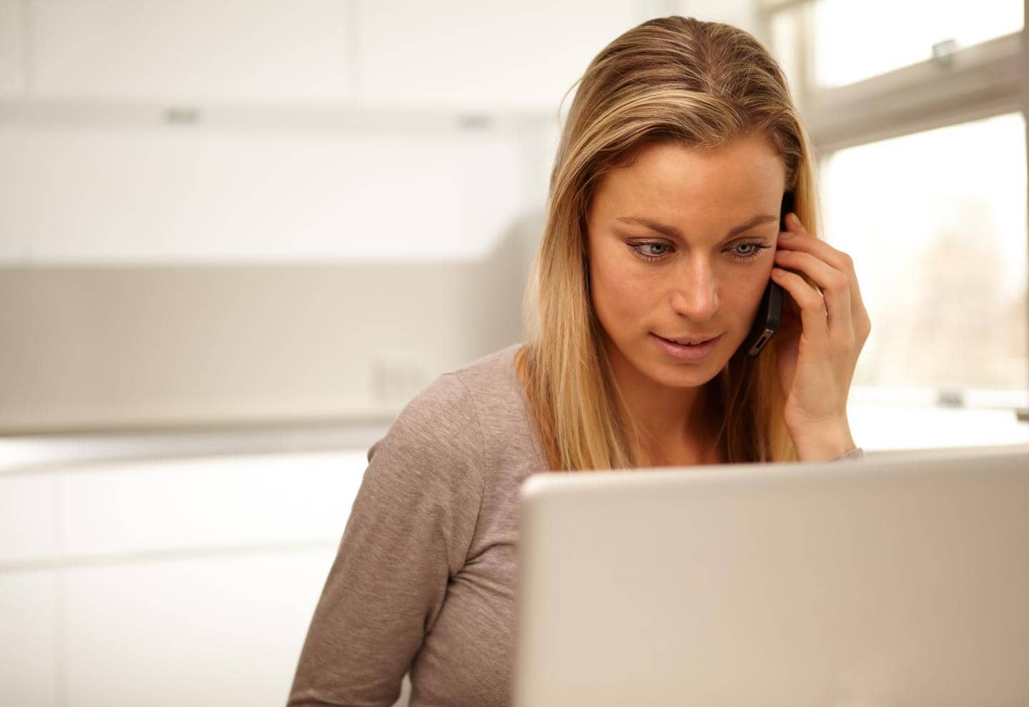Kvinde, der sidder ved sin bærbare computer og taler i telefon